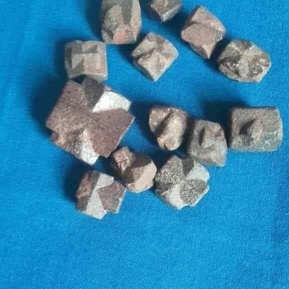 Petites pierres taillées en forme de croix, ramassées à Békora, présentées sur un tissu bleu.